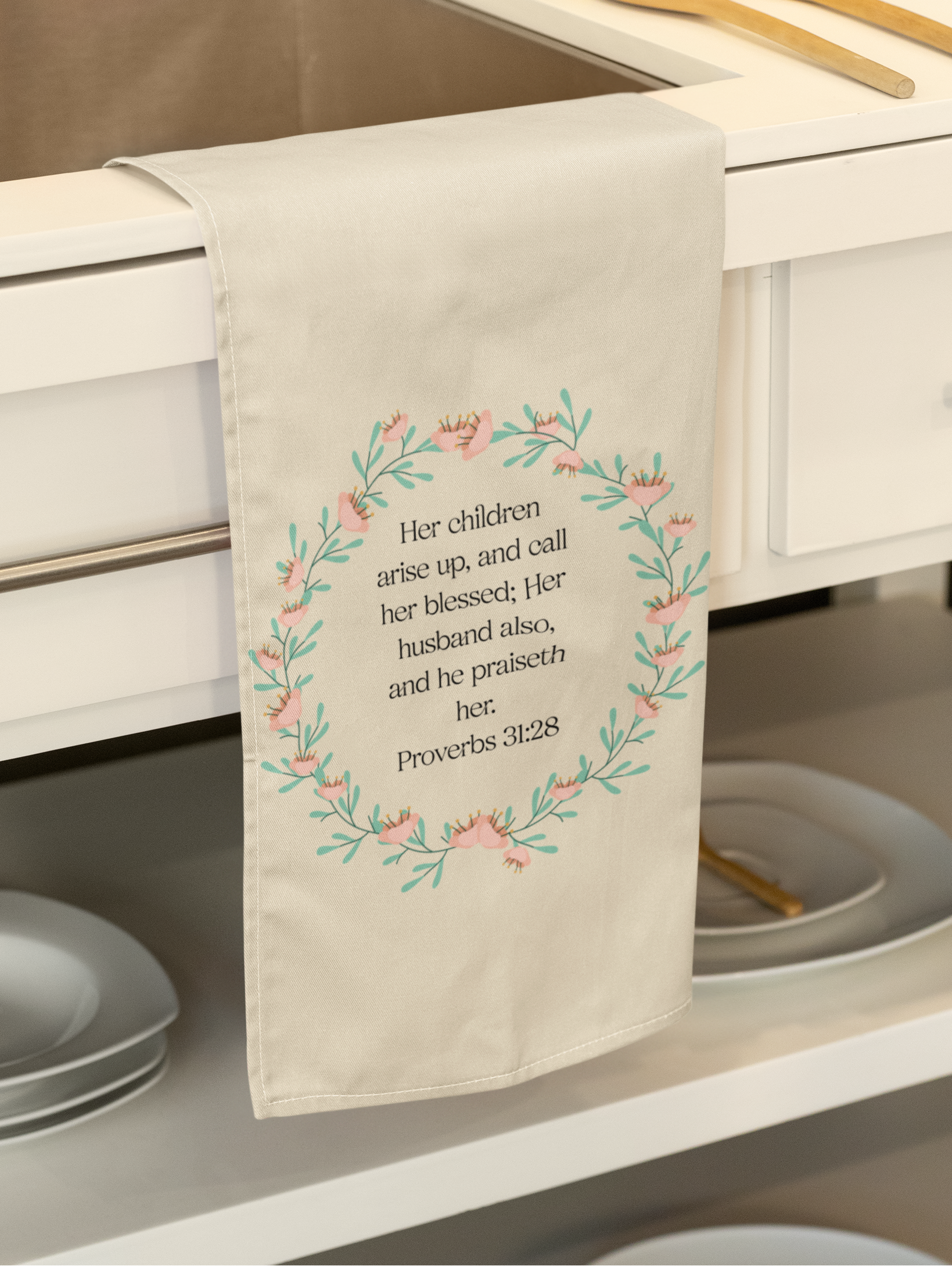 A beige cotton tea towel with a floral design and an inspirational quote, hanging on a oven handle.